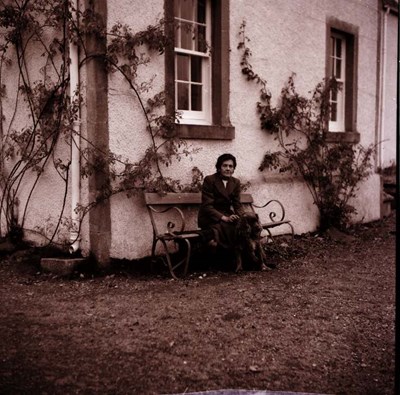 Lady seated on a bench with a dog outside a house