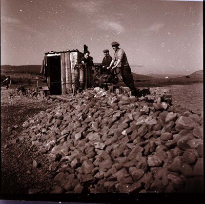 Three men standing with equipment by rubble possibly at a quarry.