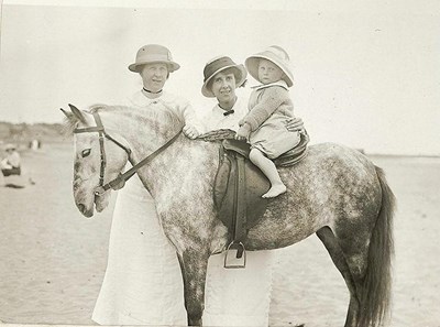Two ladies, with a baby on horse at seaside